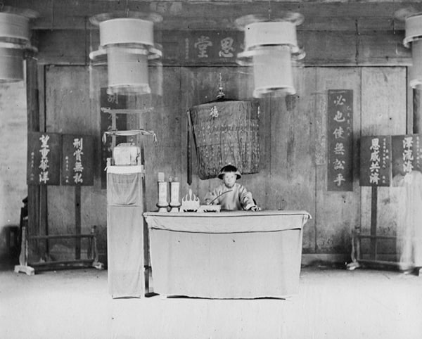 约1900年，上海县知县黄承暄，身后有万民伞，桌上除文房四宝以外还有“皂快”和“行杖”两个筒，旁边架子上是官印