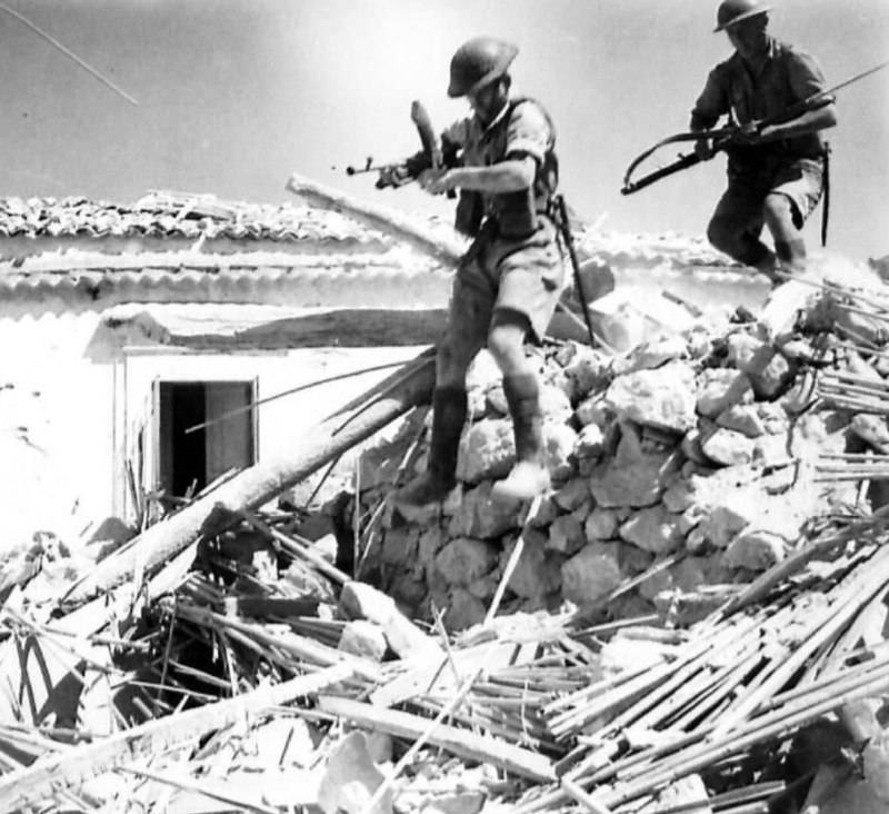 1943年7月18日，一个英军轻机枪组的两名士兵路过意大利西西里岛某个小镇