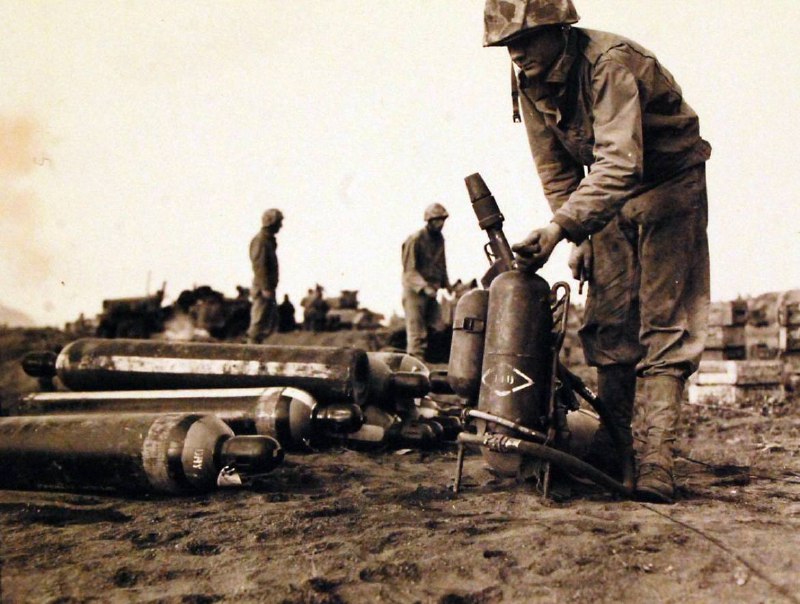 1945年，硫磺岛战役中，美国陆军一等兵托马斯·布朗（Pfc. Thomas Brown）正在为他的火焰喷射器重新加注燃料，为继续作战做准备