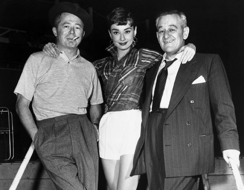 #名人 1954 年 1 月 1 日，奥黛丽·赫本在派拉蒙影业和导演她的好莱坞电影的两名男子之间摆出漂亮的姿势