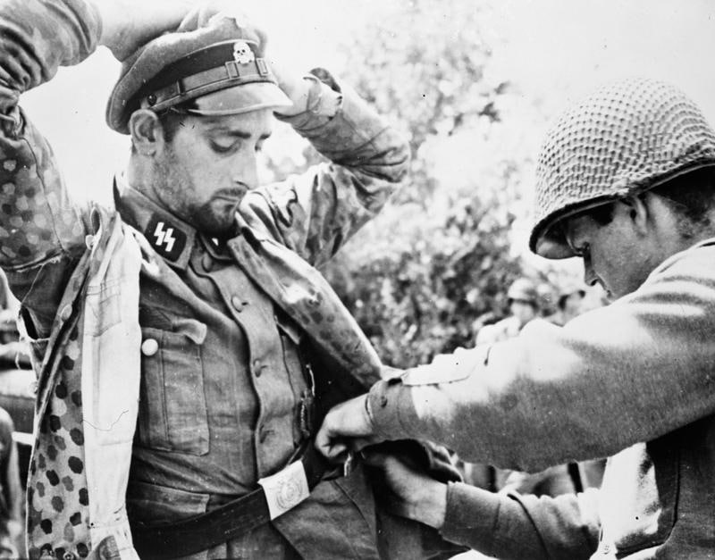 1944年，在法国加夫雷郊外，一名身穿狙击服的党卫军士官被一名美国陆军中士搜身