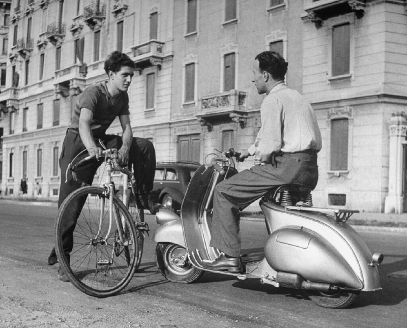 1948 年，一名摩托车骑手和一名骑自行车的人在意大利的街道上聊天